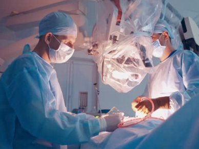 Surgeons in full surgical attire perform an operation under bright lights in a sterile operating theatre.